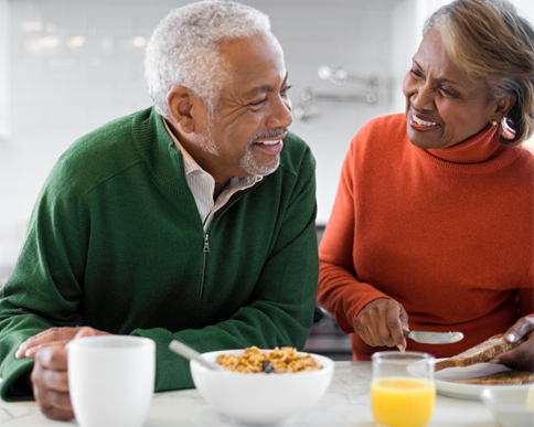 Picture of a senior couple, talking and laughing while eating breakfast